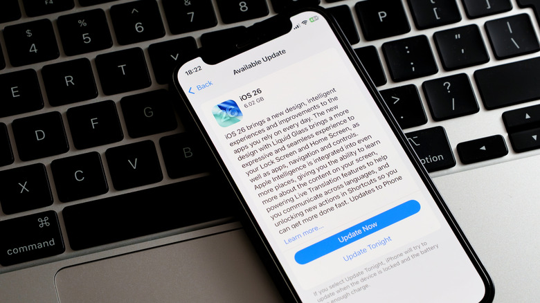 iOS 26 update on iPhone resting on MacBook keyboard in light mode