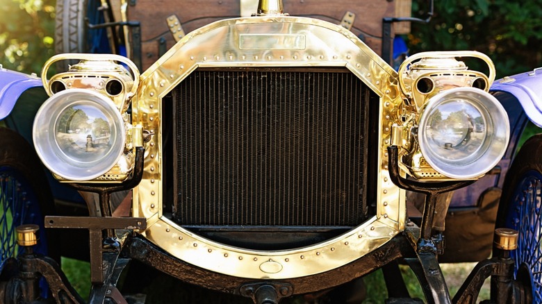 Front grille of a gold 1907 car with old acetylene headlamps