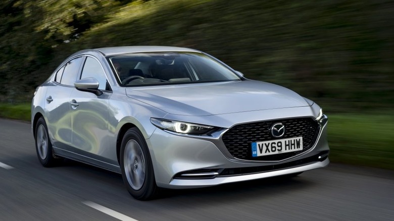 Front right view of silver Mazda 3 on tree-lined road