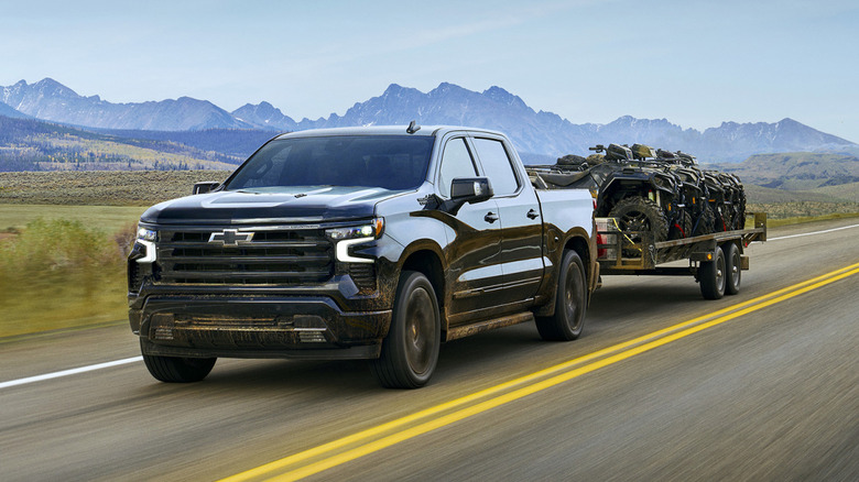 A black Chevrolet Silverado towing multiple ATVs on a remote U.S. highway.