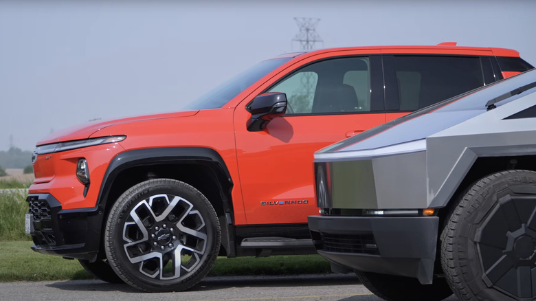 A front side profile view of a red Chevrolet Silverado and a gray Tesla Cybertruck parked side by side.