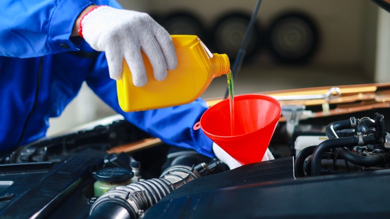 A mechanic wearing gloves pouring oil into a car during an oil change