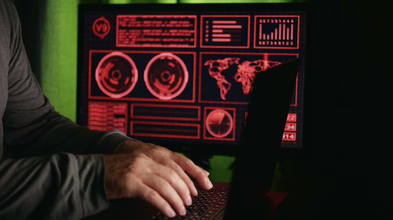 A man typing on a laptop with a red UI in the background