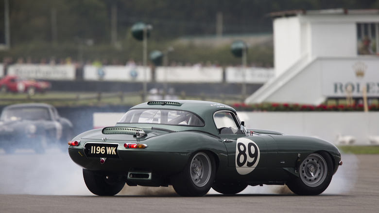 Classic 1963 Jaguar E-Type race car spinning the tires at racing circuit, rear-right three-quarter view