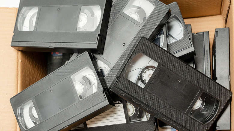 A pile of VHS tapes in a cardboard box.