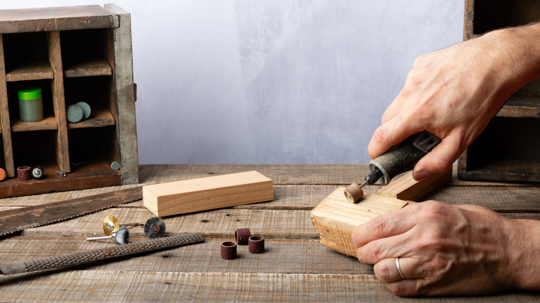 Two hands use rotary tool while woodworking on wood table