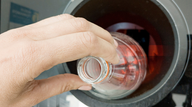 Hand placing a bottle in a reverse vending machine.