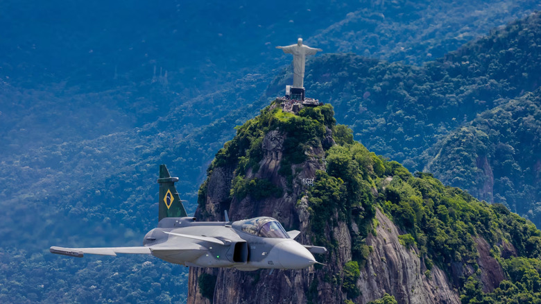 Brazilian Gripen E flying past Christ the Redeemer statue on mountaintop