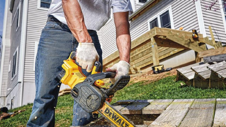 Man in jeans cutting an old deck with a Dewalt chainsaw