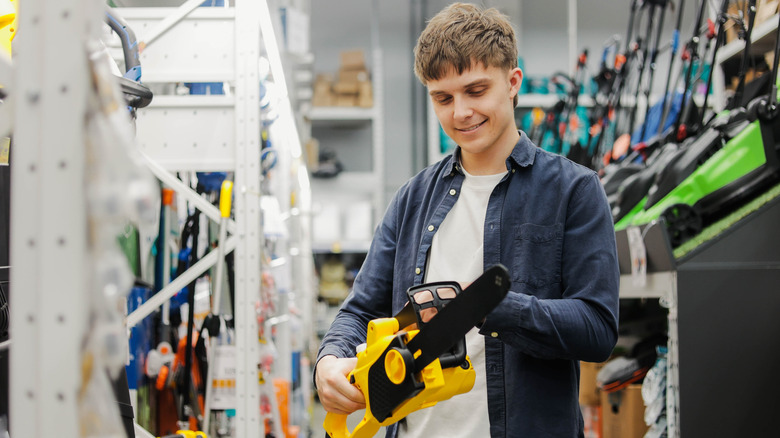 Young man holding yellow chainsaw in hardware store