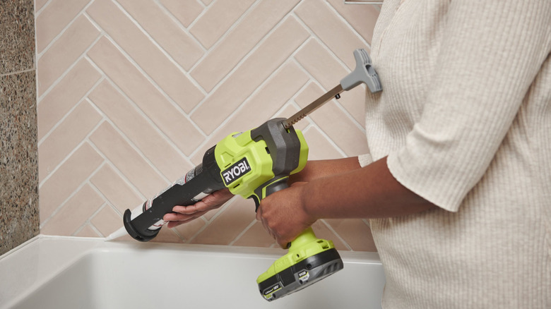 A person using a Ryobi caulk gun to apply caulk around a bathtub