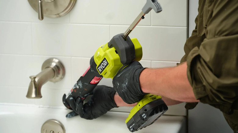A person in a green shirt using a battery-powered Ryobi caulk gun to seal a sink
