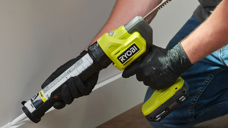A person using a Ryobi caulk gun to seal a part of a wall