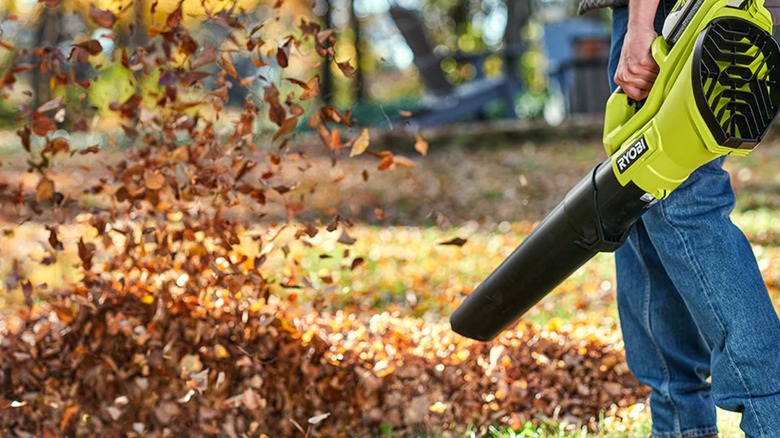 A worker using a 40V Ryobi blower on a leaf pile.