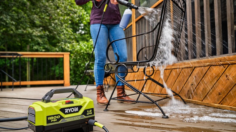 A lady using a portable pressure washer to clean a chair