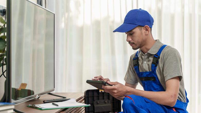Technician checking or setting up television with digital tablet