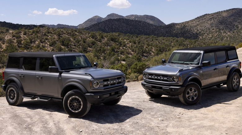 Two 2025 Ford Broncos parked beside each other on sand; front-right and front-left 3/4 views