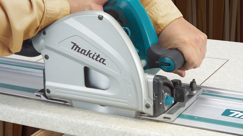 close-up of person using a corded Makita track saw to cut wood