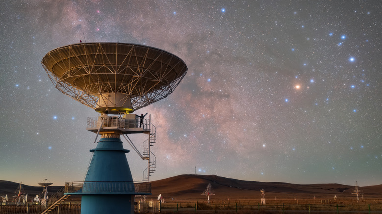 A radio antenna array pointed directly up with stars and an arm of the Milky Way visible in the background