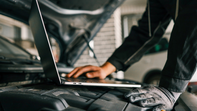 A mechanic using a laptop on a car engine for diagnostics in a garage