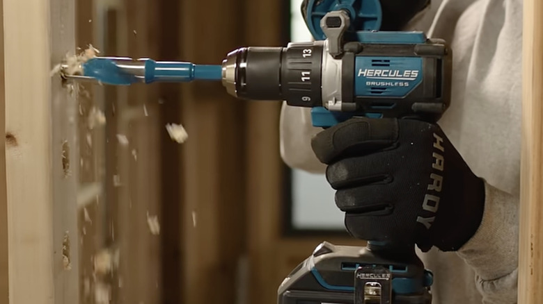 gloved hand holding Hercules drill and making hole in wall stud