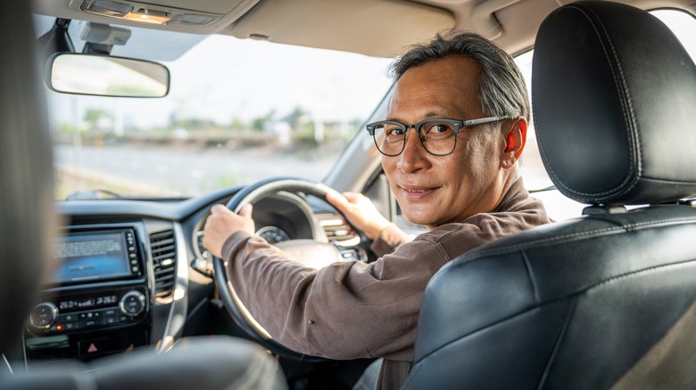 An older Asian origin man behind the wheels of a car.