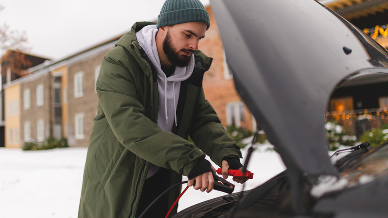 Young man with a beard trying to jump start his car in the winter since the battery is dead