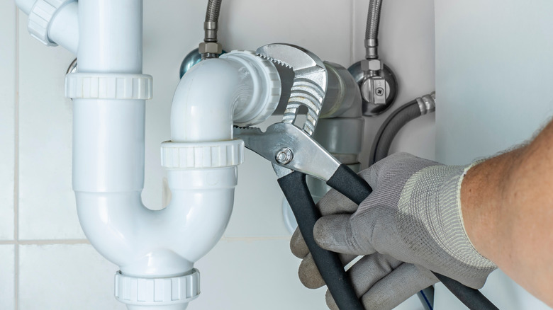 A person using pliers to tighten a P-trap