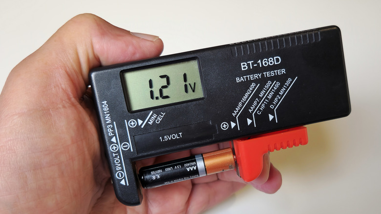 Hand holding a battery tester with AAA connected