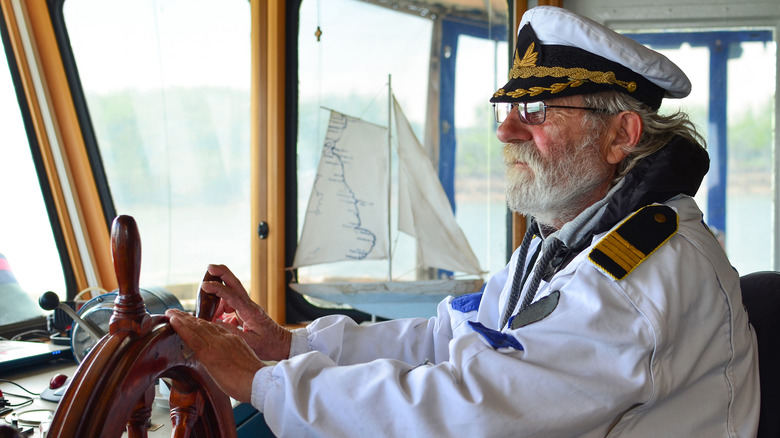 A captain with long grey hair at the wheel of his boat.