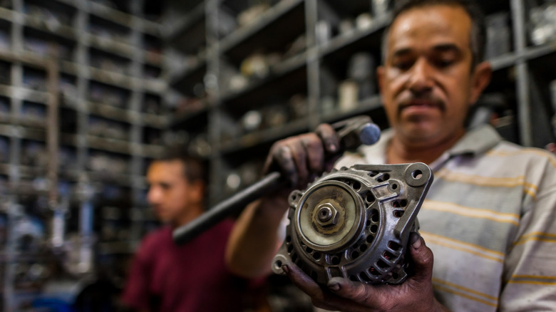 Mechanic holding the alternator of a vehicle.