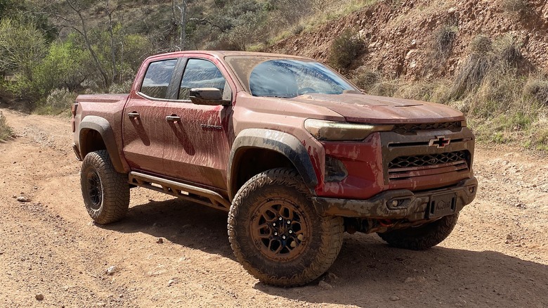 Red Chevrolet Colorado parked off-road and covered in mud