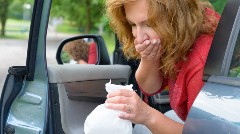 Person leans out of car holding sickness bag.