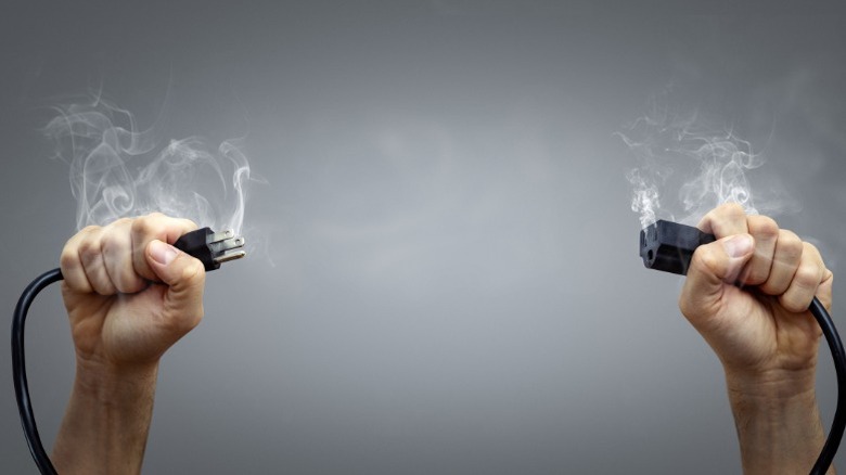 Hands holding smoking electrical plug and socket