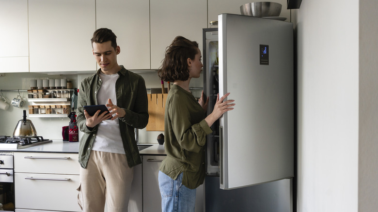 Two people standing in kitchen, one opening refrigerator