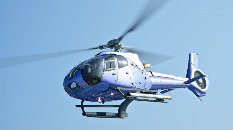 A small blue private helicopter flying through clear skies.