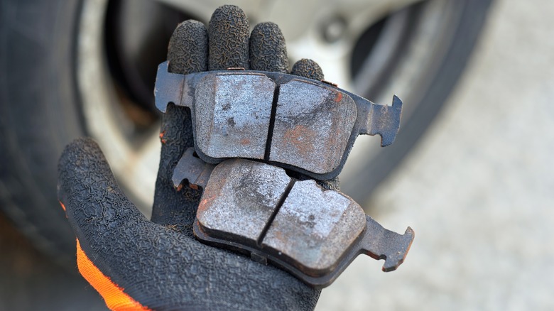 A gloved hand holding two brake pads