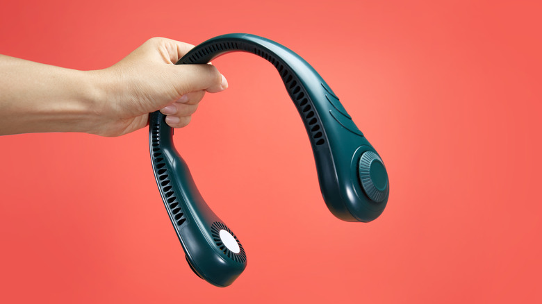 A person holding a neck fan against a red background