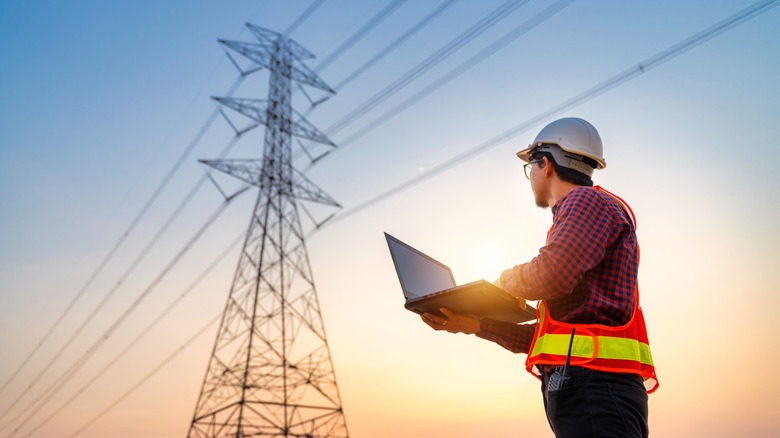 An electrician with hard hat and vest looking up at power lines.