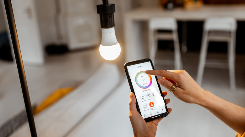 Woman using app on smartphone to control smart bulb