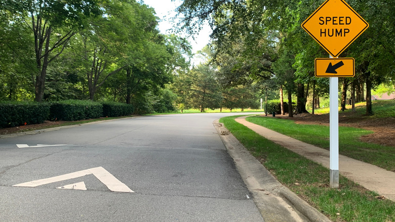 A yellow "speed hump" sign on a grassy sidewalk next to a speed hump