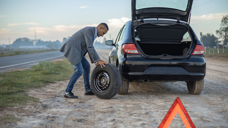 Man changing a tire on the side of the road