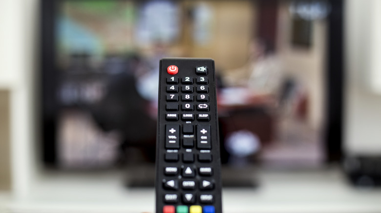 A generic remote held up in front of a blurred TV screen
