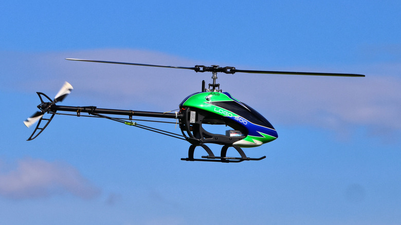 A green RC helicopter flying against a blue sky