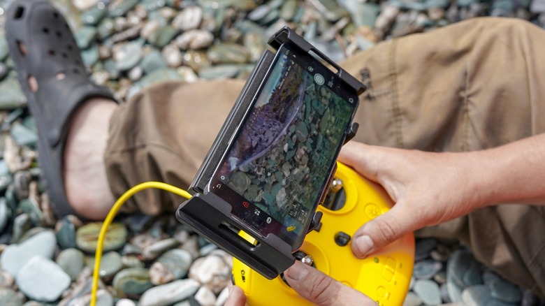 Biologist viewing drone footage on a yellow controller while sitting at a bank
