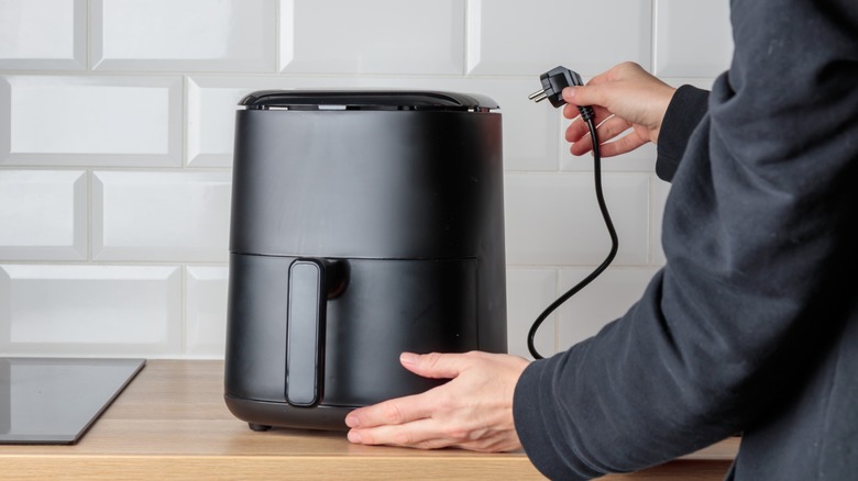 Black air fryer on wooden kitchen counter bring unplugged by a person in a black coat