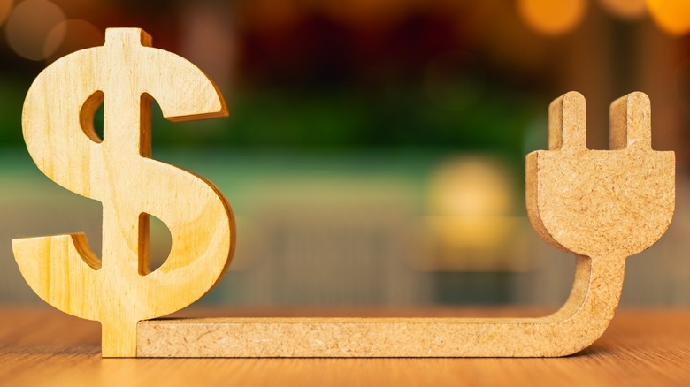 Wooden carving of a dollar sign connected to an electric plug