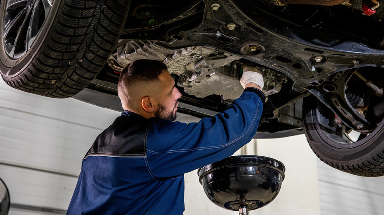 Mechanic draining oil from car engine