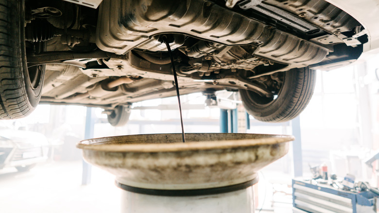 Draining old engine oil into pan with car on lift
