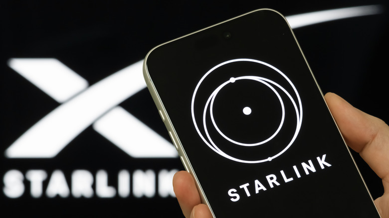 A person holds a smartphone displaying the Starlink logo,